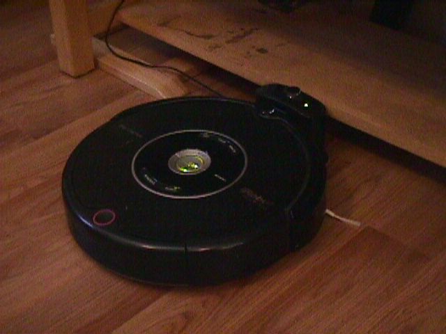 photo of my roomba taken on a mavica FD7. it's a grainy picture of a black circle on a blond faux wood floor