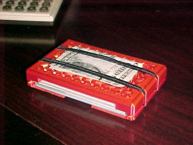 A grainy picture of the wallet on my desk. It has one dollar bill strapped to it and is full of cards. there is a calculator in the background.